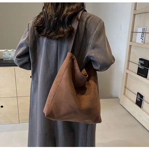 Side view of large brown faux suede tote bag worn over a charcoal wool coat for daily work