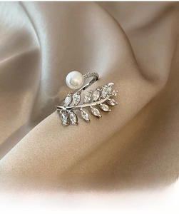 Dettaglio anello foglia argento con zircone e perla su sfondo di seta marrone