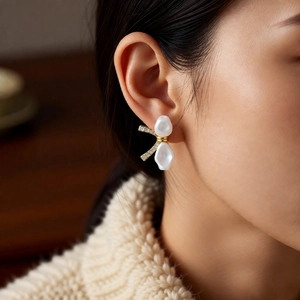 Close-up of 18k gold plated bow earrings with baroque pearls and crystals on a model
