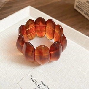 Macro shot of amber resin wide elastic bracelet with tortoiseshell patterns on white tray