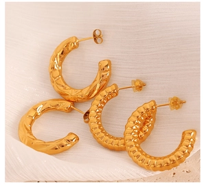 Macro shot of three pairs of textured gold C-shaped hoop earrings on white draped fabric