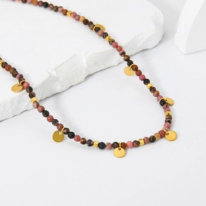 Collana di perline multicolore con ciondoli dorati su espositore in marmo bianco