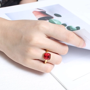Minimalist gold titanium ring with a large red square zircon worn on a hand over a magazine
