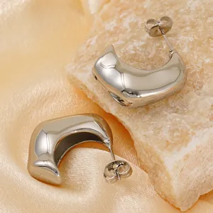 Polished silver titanium steel C-shaped stud earrings on beige stone and silk backdrop