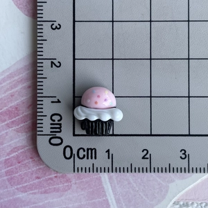 Detailed view of a mini 1cm resin cupcake charm with scale reference on a cutting mat