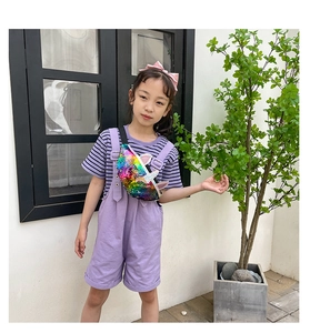 Girl wearing a colorful sequin unicorn crossbody bag with purple overalls and striped shirt