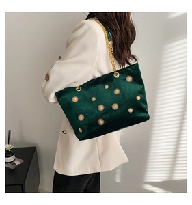 Gros plan du sac cabas en velours vert avec rivets soleil dorés et grosse chaîne en métal