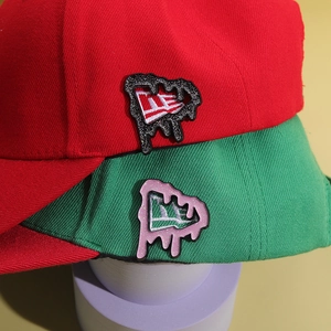 Glittering melt-effect enamel pins with NE logo on red and green baseball caps