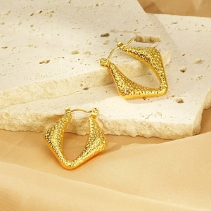 Makro-Detail goldener geometrischer Ohrringe mit Hammerschlag-Textur auf Satin