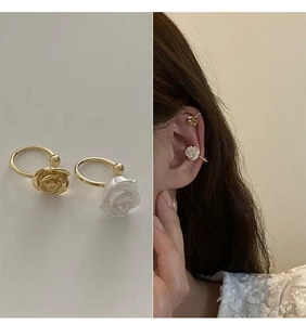 Detail of gold metal rose and white resin flower ear cuffs shown on a model