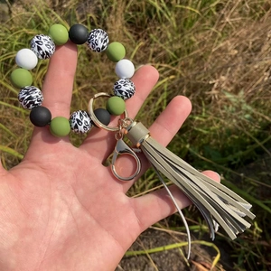Close-up of leopard print silicone bead keychain with olive tassel on green grass