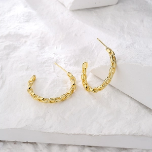 Exaggerated C-shaped gold chain hoop earrings with cubic zirconia on stone background