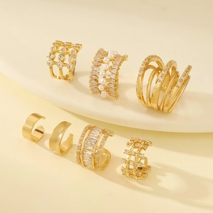 7-piece gold ear cuff set with rhinestones and pearls on beige display stand