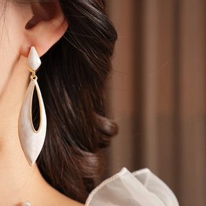 Close-up of a white enamel water drop earring with golden trim on model's ear