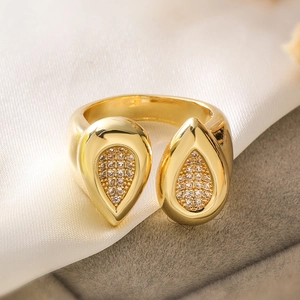 Detailed close-up of double pear-shaped gold ring with pave zircon on white silk background