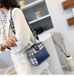 Close-up of model wearing blue plaid bucket bag with wide strap and leather stitching
