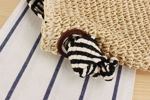 Detail of paper straw bag showing beige woven texture and striped knotted rope strap