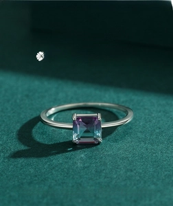Macro view of minimalist silver ring with square gradient paraiba stone on dark green background