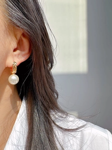 Detailed close-up of quilted gold metal earrings with a large white hanging pearl