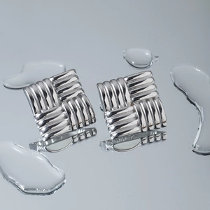 Macro detail of square silver earrings featuring a textured woven pattern and 18k finish
