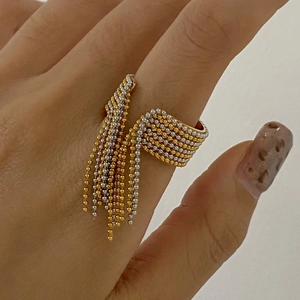 Detailed view of woven metal bead ring with long dangling gold and silver tassels