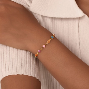 Close-up of colorful heart charms on a gold chain bracelet worn on a female wrist