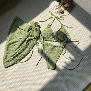 Detailed view of sage green textured bikini set with sarong on a beach-themed background