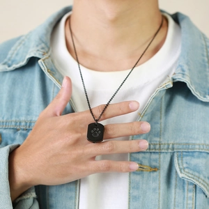 Close-up of a black stainless steel urn necklace with a paw print worn by a male model