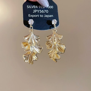 Detailed close-up of gold layered ginkgo leaf earrings held on a black 925 silver card