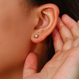 Macro shot of gold four-prong set round zircon stud earring worn on ear