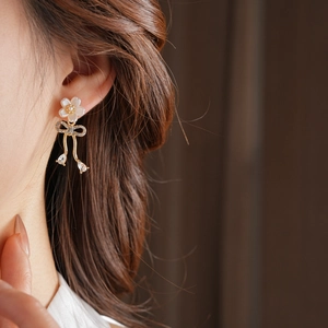 Gros plan de boucles d'oreilles fleur dorée avec nœud et perles sur un modèle élégant