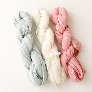 Detail of soft pleated long scarves in light blue, beige, and rose pink with fringe edges