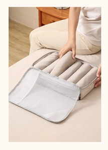 Detailed view of placing folded clothes into a mesh travel organizer bag in beige