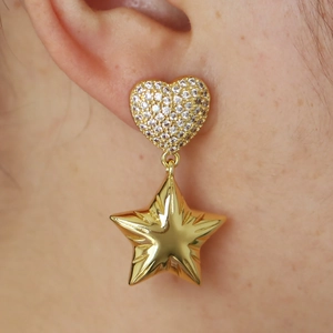 Close-up of gold-plated heart and star earrings with pavé zircon settings on a model