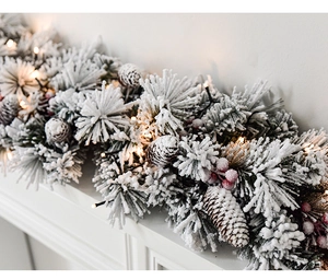 Close-up of snowy Christmas garland with pine cones, red berries and warm LED lights