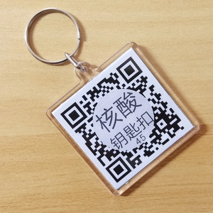 Square acrylic QR code keychain with silver metal ring on light wood texture background