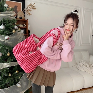 Pink and red striped plush tote bag being worn by a model near a festive Christmas tree