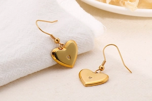 Detail of polished gold heart earrings with zircon inlay on white fabric background