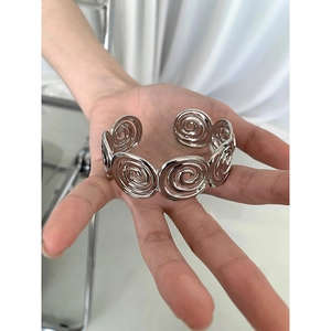 Detail view of a silver spiral disc bangle with vintage geometric texture on a person hand