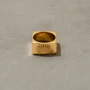 Détail macro d'une bague carrée dorée en acier inoxydable avec motif coquillage