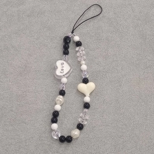 Macro detail of beaded phone charm featuring black and white acrylic heart-shaped beads