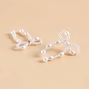 Detail view of handmade bow-shaped earrings featuring cream imitation pearls and gold pins