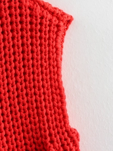 Close-up of bright red chunky knit vest texture with thick yarn stitching patterns