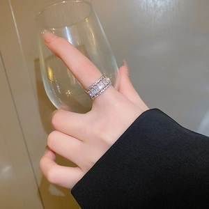 Detail of silver wide band zircon ring on finger holding glass with warm lighting