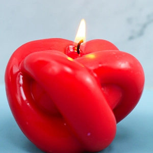 Gros plan d'une bougie parfumée en forme de nœud rouge allumée avec une flamme vive