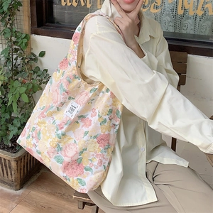 Dettaglio della borsa tote in tela a fiori indossata da una modella in un caffè accogliente