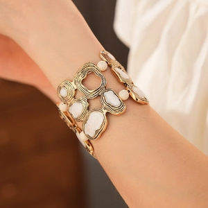 Close-up of a wide vintage geometric metal bracelet with white enamel and bead accents