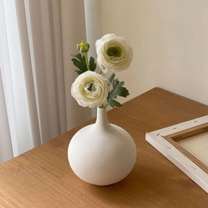 Moderne weiße Keramikvase in Kugelform mit feinen Rillen und Kunstblumen auf einem Holztisch