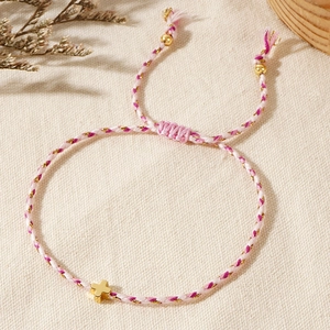 Detail of a handmade braided cotton bracelet with a gold cross pendant and soft pink tones