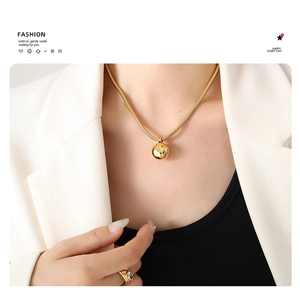 Close-up of a polished gold spherical pendant on a sleek snake chain worn by a model